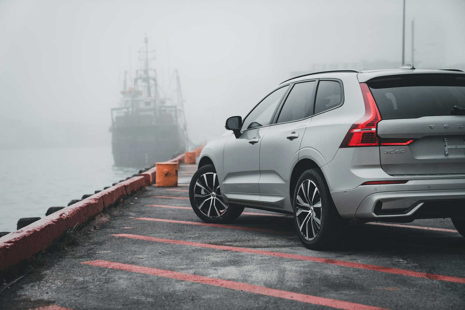 A sleek Volvo XC60 parked by a foggy harbor, with a ship in the background, creating a mysterious and serene atmosphere.